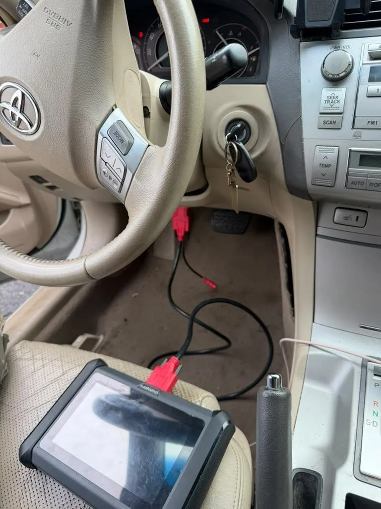 Car interior with a key in the ignition and a programming tablet connected below the dash.